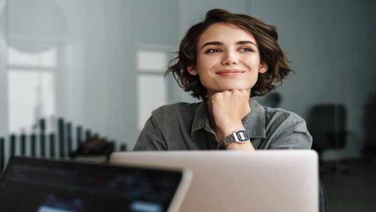 Image of young beautiful joyful woman smiling while working with laptop in office.