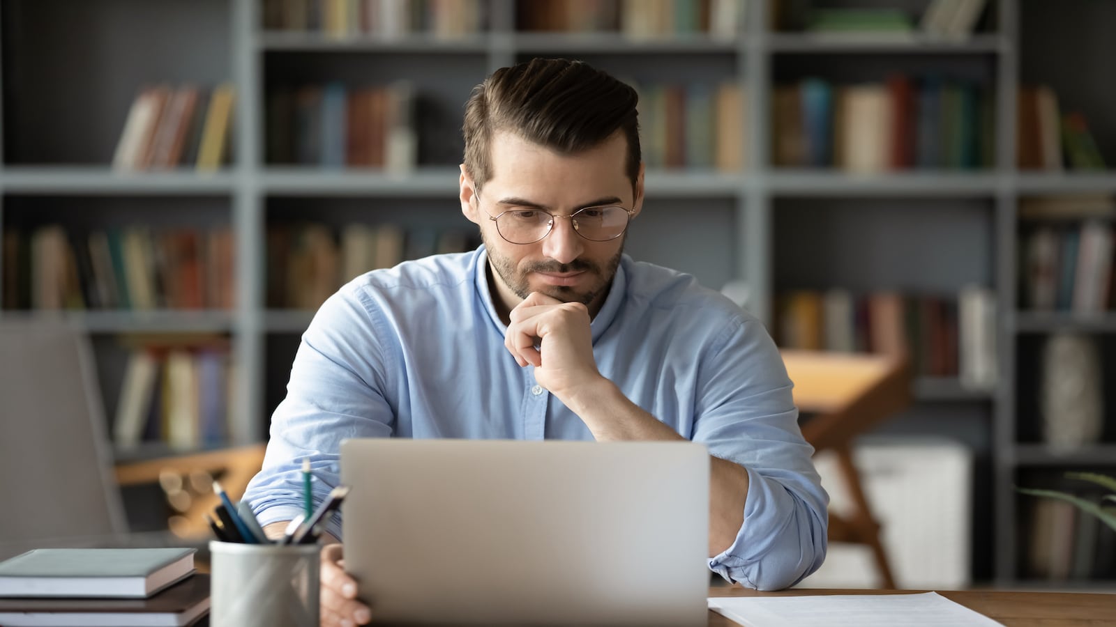 Thoughtful young businessman in eyeglasses looking at computer screen.