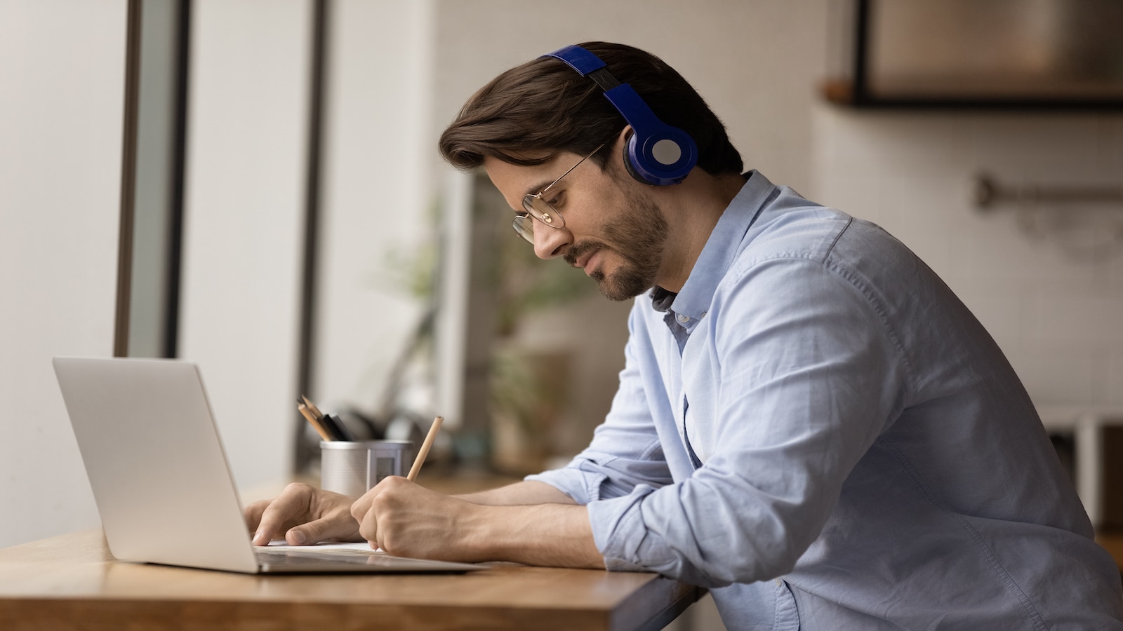 Man writing with left hand at computer listening to headphones music.