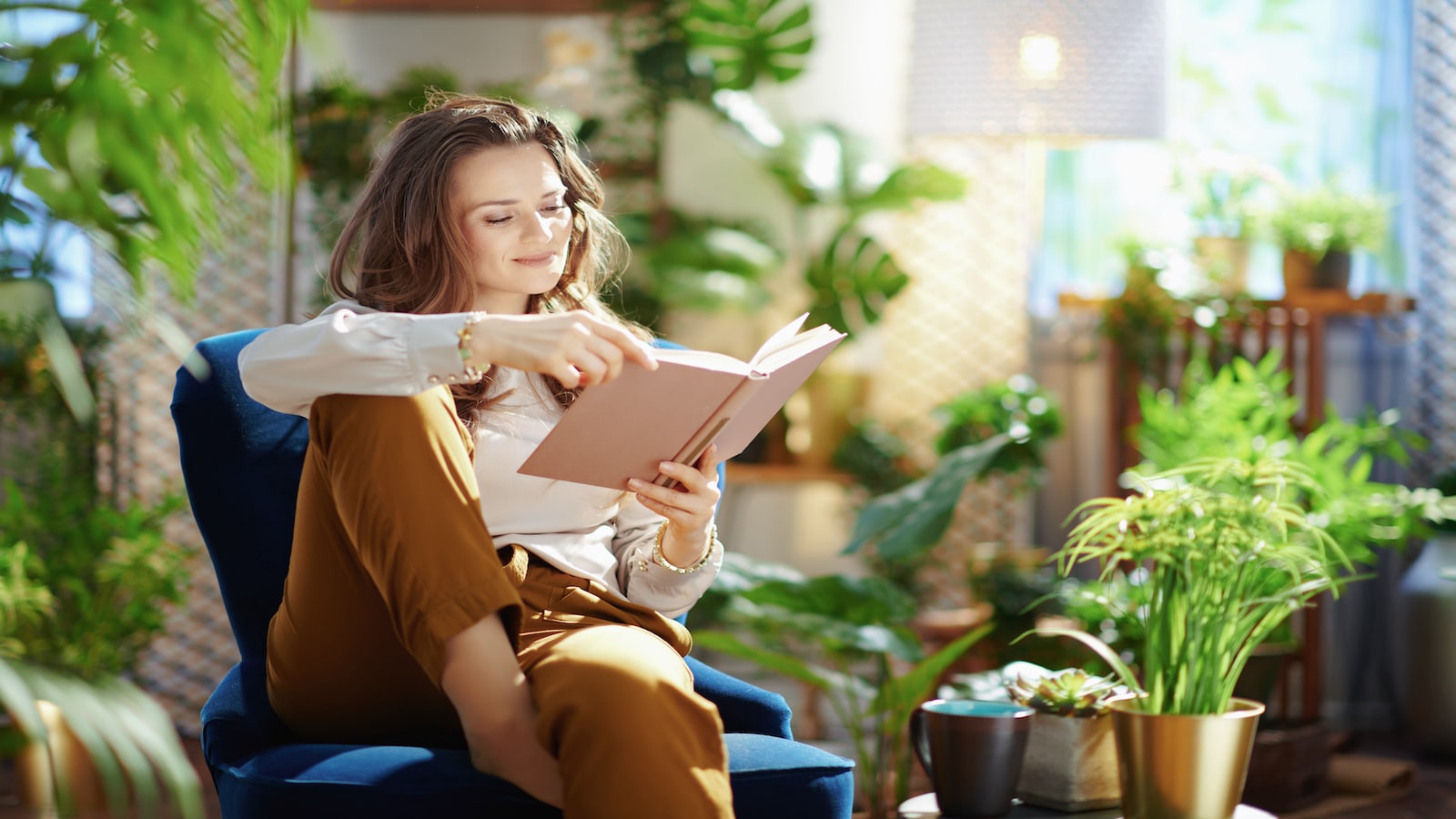 Woman relaxing reading book in house with alot of plants.