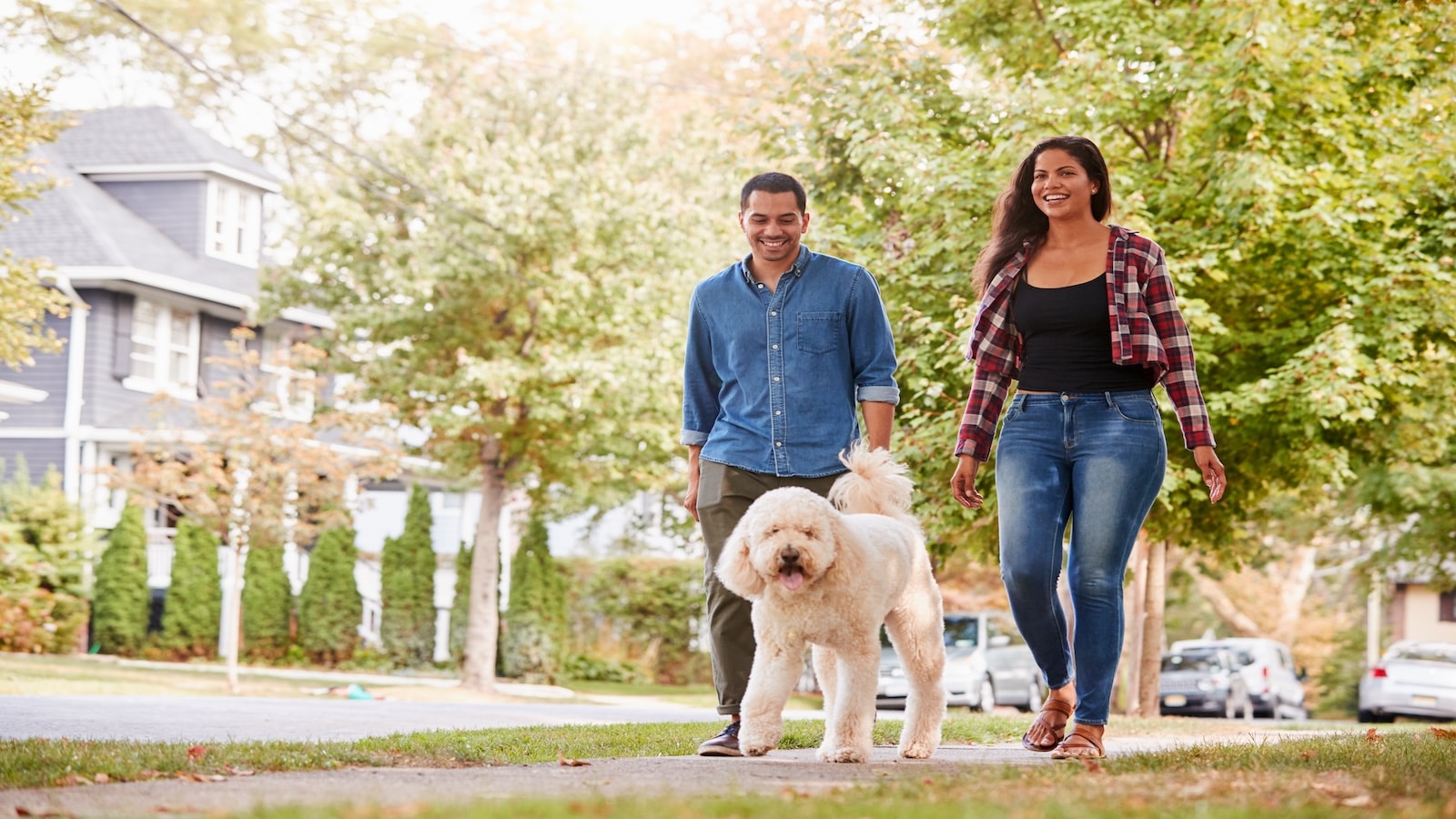 Couple Walking Dog Along Suburban Street.