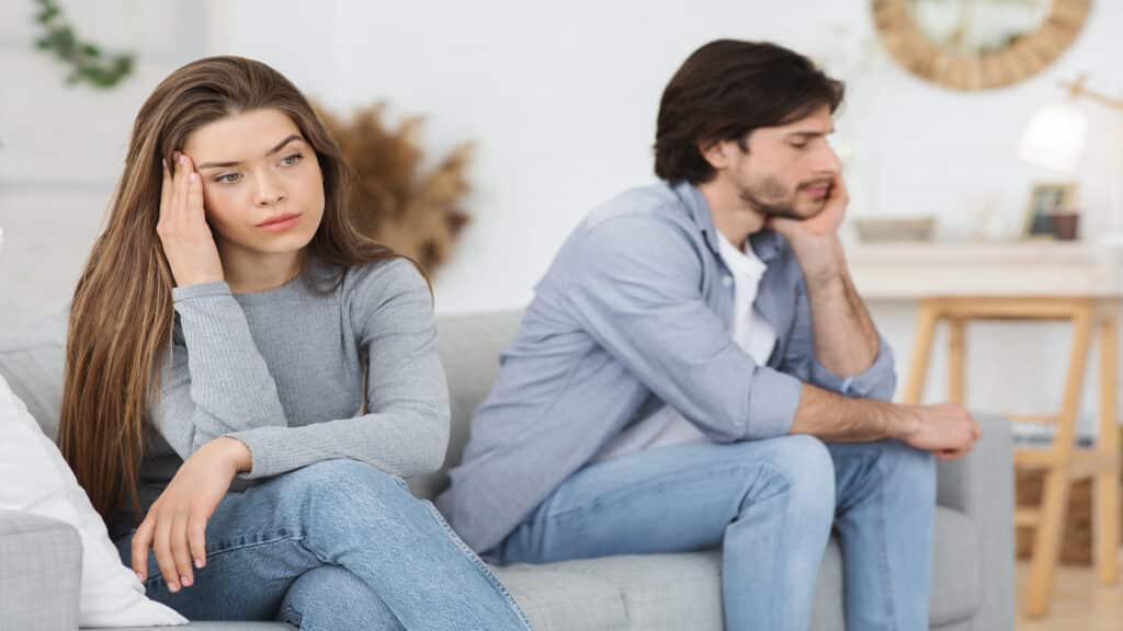 Upset young couple sitting on sofa at home, having conflict.