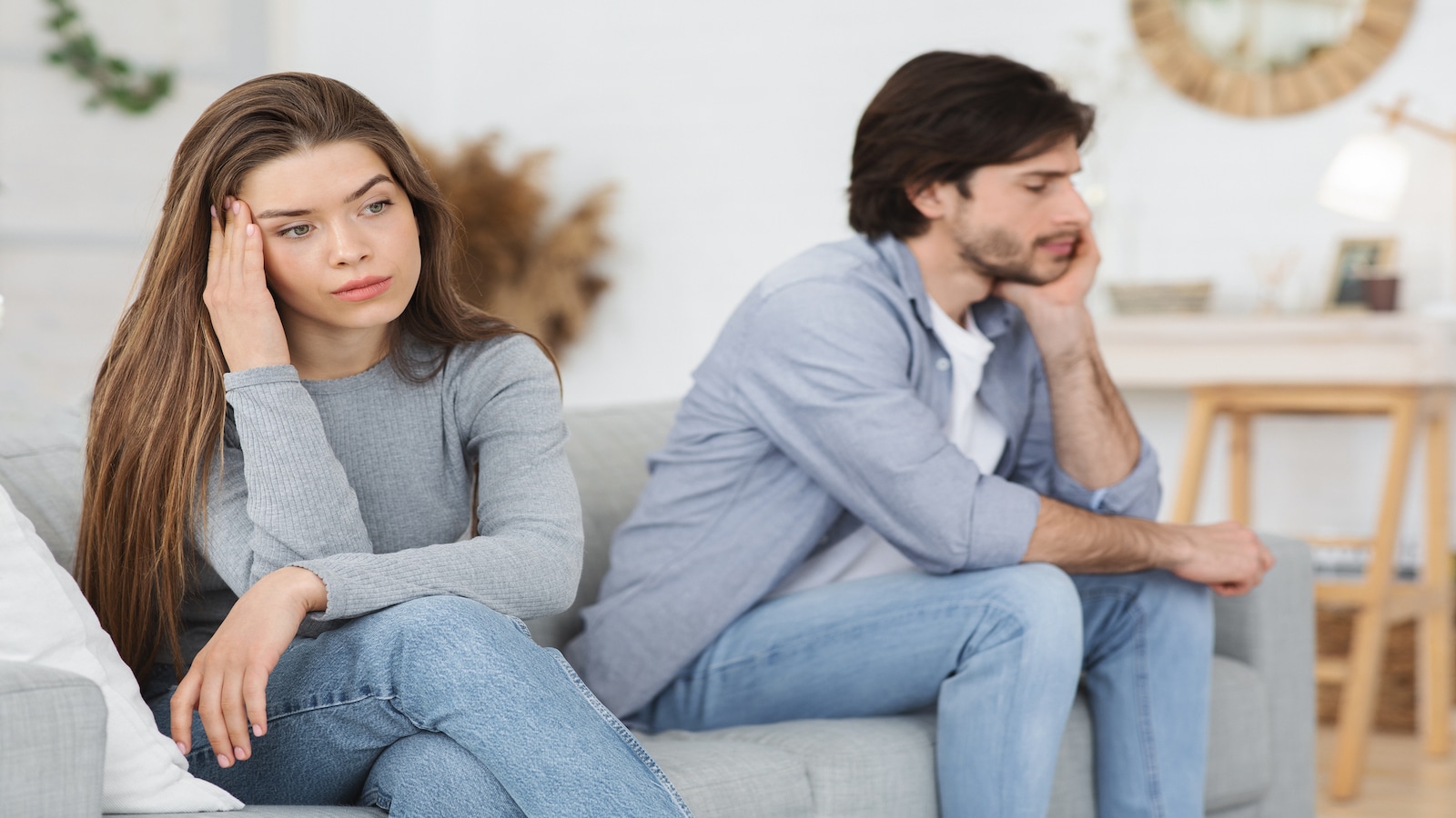 Upset young couple sitting on sofa at home, having conflict.