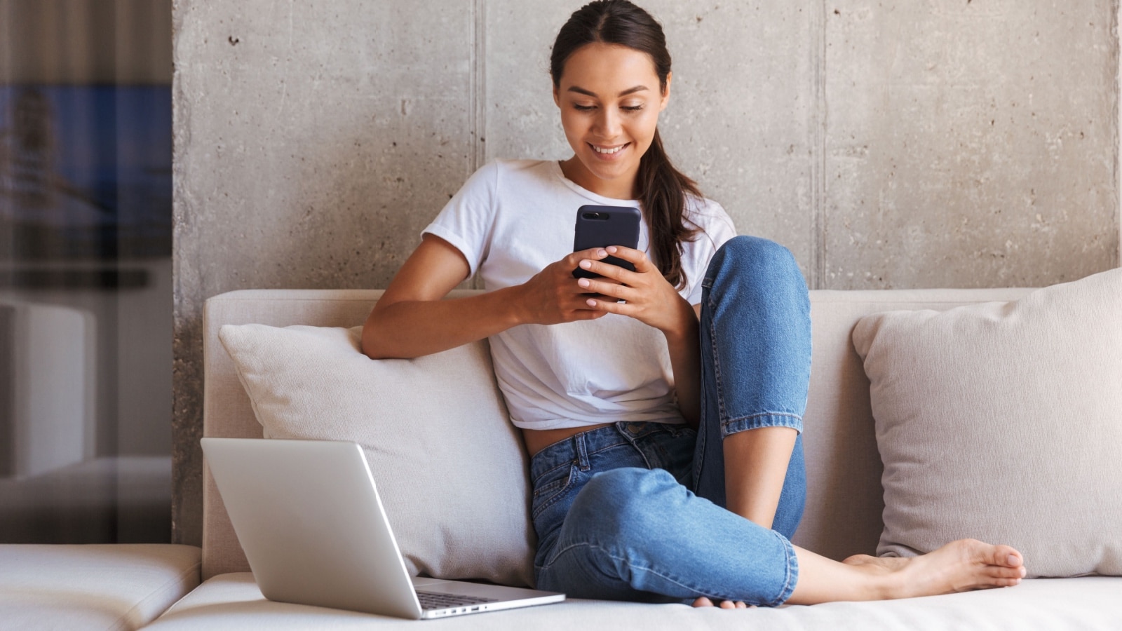 woman sitting on couch scrolling on phone smiling happy.