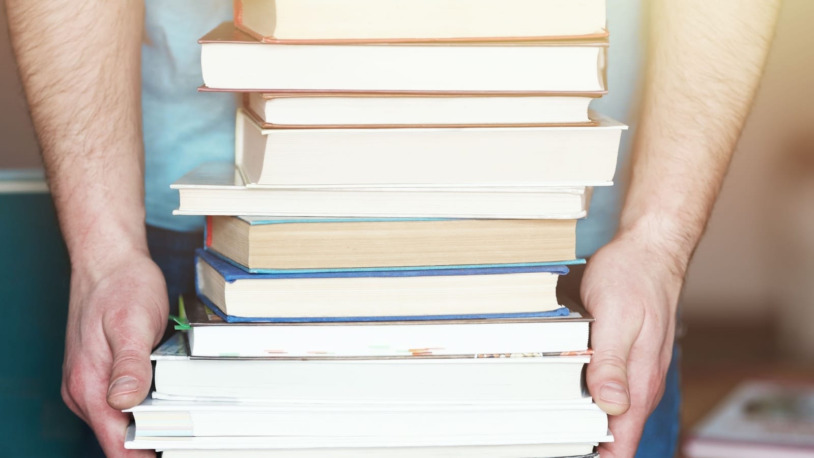 A man holds a stack of books in his hands. A photo without a face. A lover of reading. Close-up.