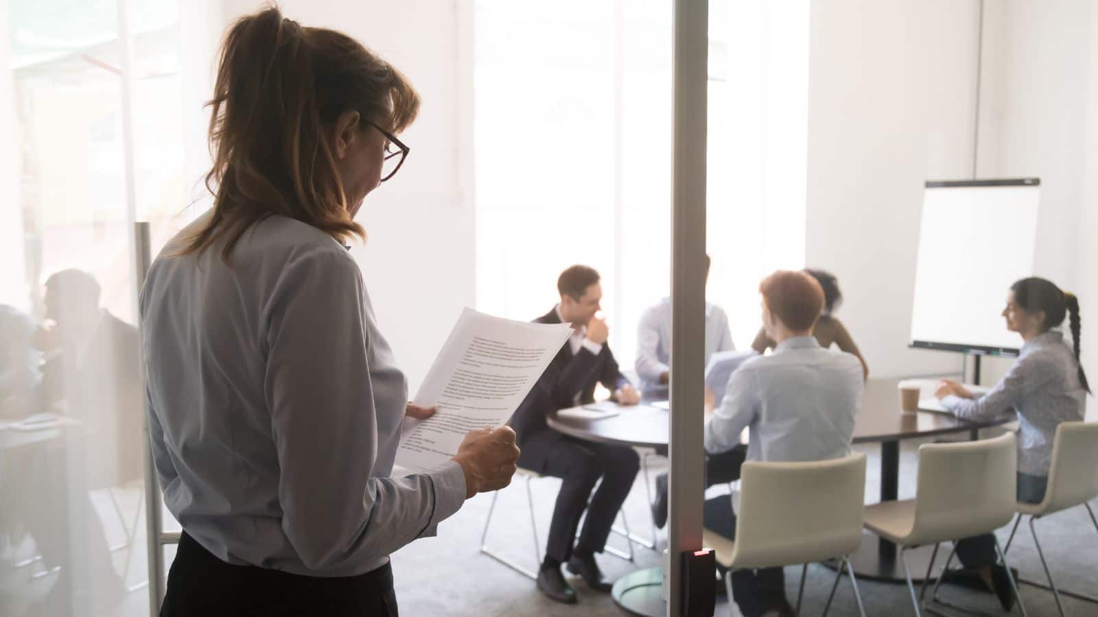 A woman standing at the office door feeling worried before a meeting.