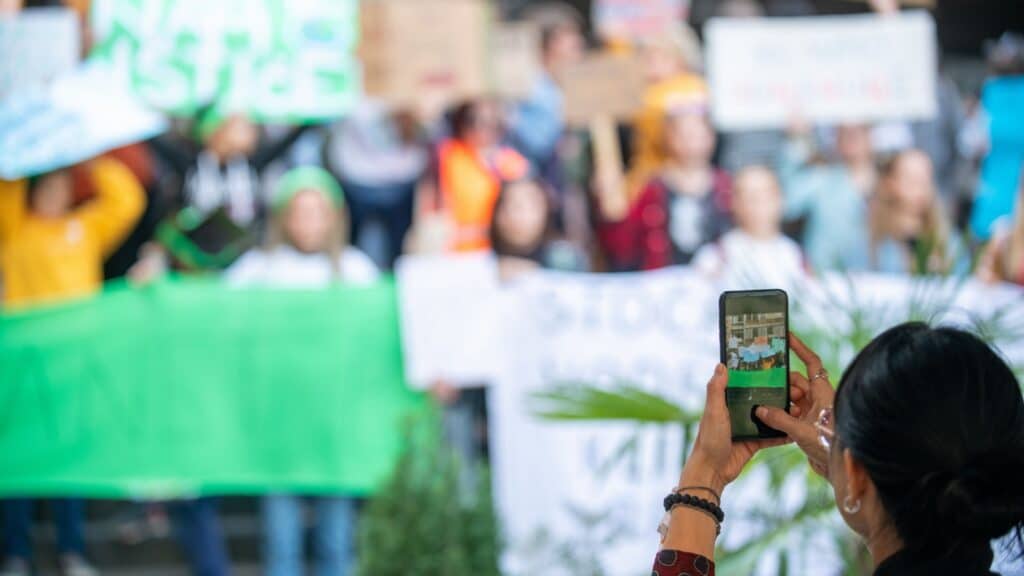 Climate Change Protest on the Street. Focus on Woman Holding Phone and Recording Protest.