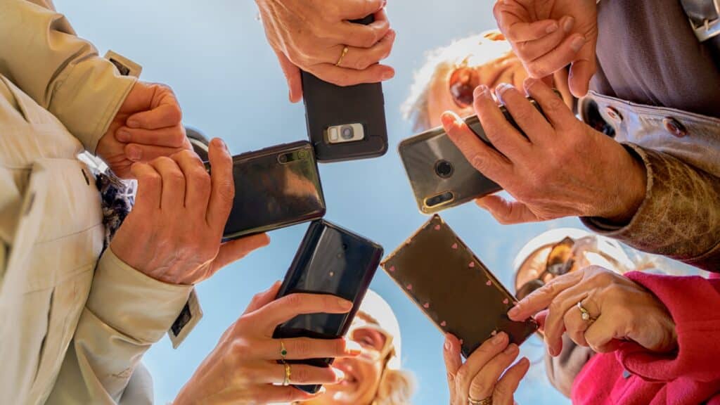 Friends group of all ages holding and using smartphones. View from below. Hands with mobile phones - Technology concept.