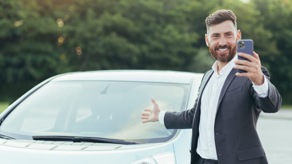 Successful and happy man brags about buying a new car, having fun talking to friends uses a video call in the phone app.