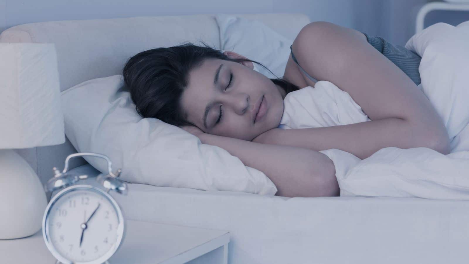 Woman asleep with an alarm clock by the bedside.