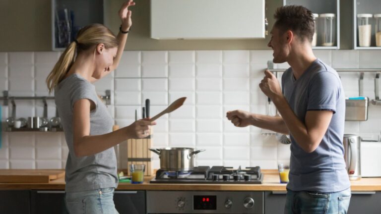 Funny young couple dancing to music together enjoying cooking in the kitchen, man and woman in love having fun preparing breakfast food feeling happy and carefree on weekend lifestyle at home