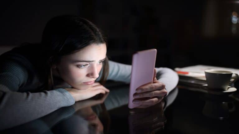 Sad female checking phone at night at home