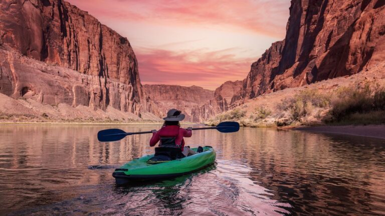 Adventurous Woman on a Kayak paddling in Colorado River. Glen Canyon, Arizona, United States of America. Sunrise Sky Art Render. American Mountain Nature Landscape Background.