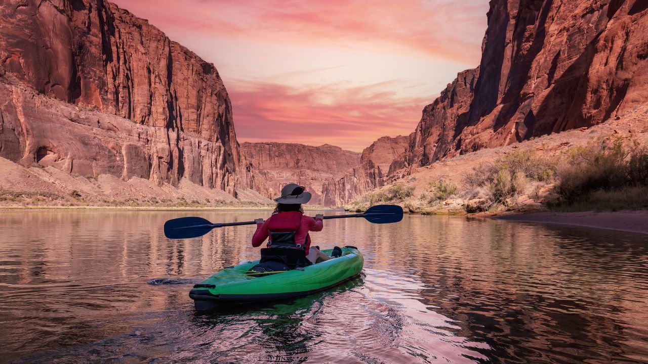 Adventurous Woman on a Kayak paddling in Colorado River. Glen Canyon, Arizona, United States of America. Sunrise Sky Art Render. American Mountain Nature Landscape Background.