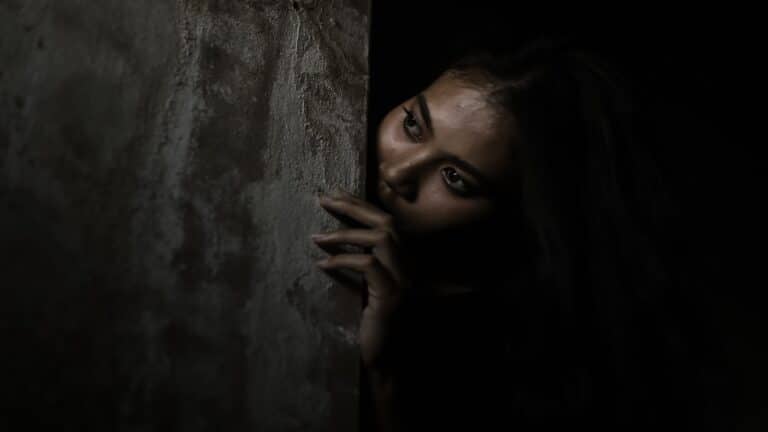scared woman hiding behind wall.