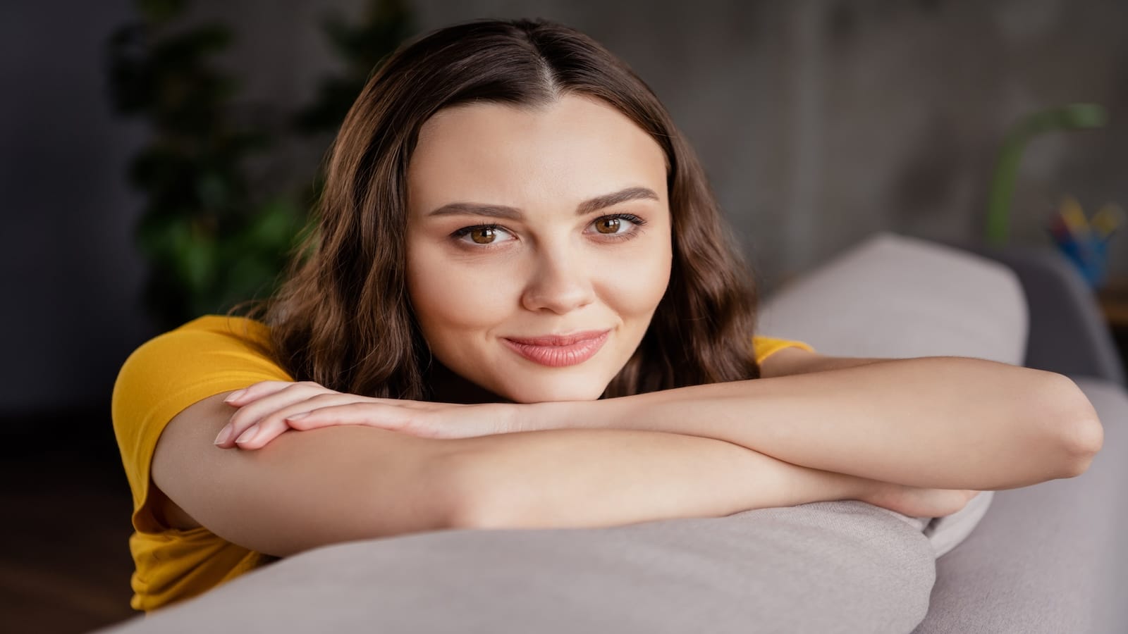 Photo of dreamy charming young woman dressed casual clothes sitting sofa smiling indoors loft apartment.
