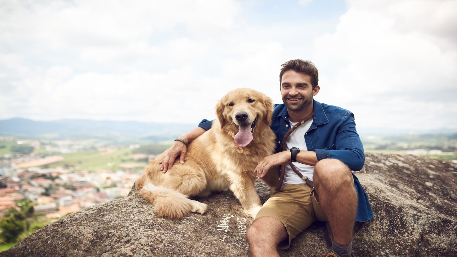 Young man sitting on a rock with his golden retriever after a day out hiking.
