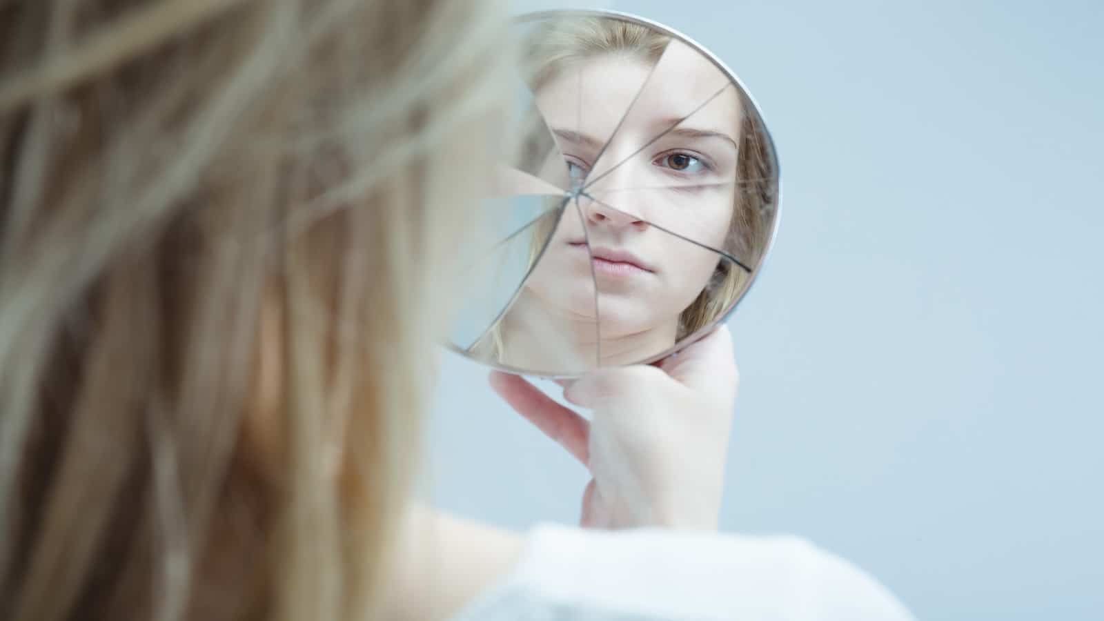 Image of woman with mental disorder holding broken mirror.