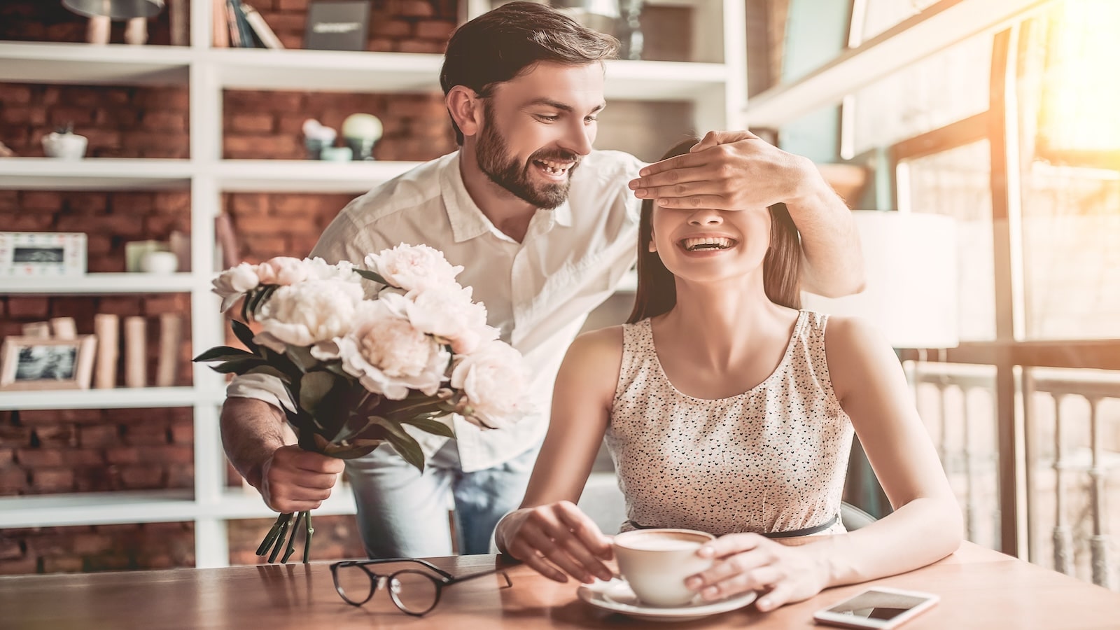 man surprising woman with roses in cafe bright sunny day.
