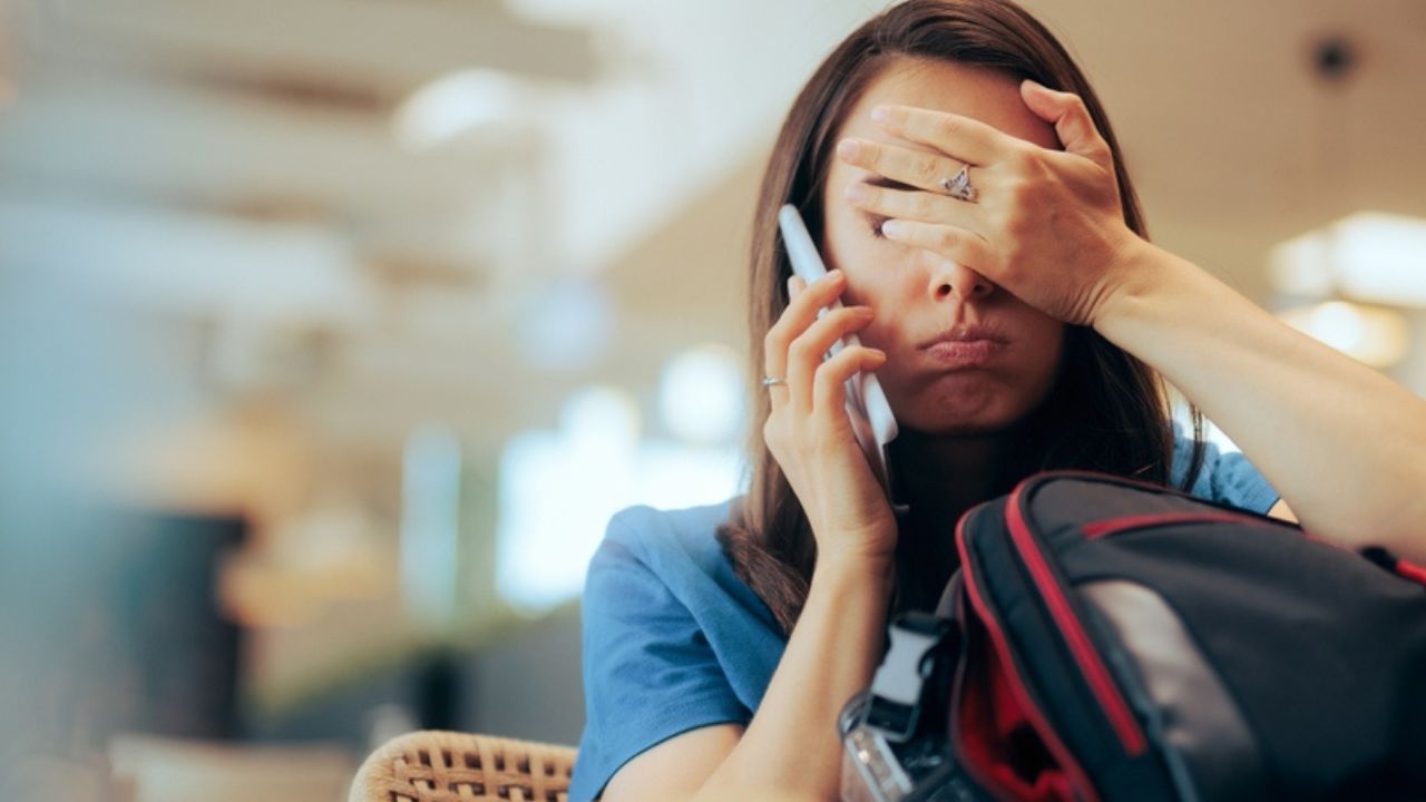 Unhappy Woman Talking on the Phone Waiting in an Airport Stressed traveler speaking on her cellphone feeling overwhelmed