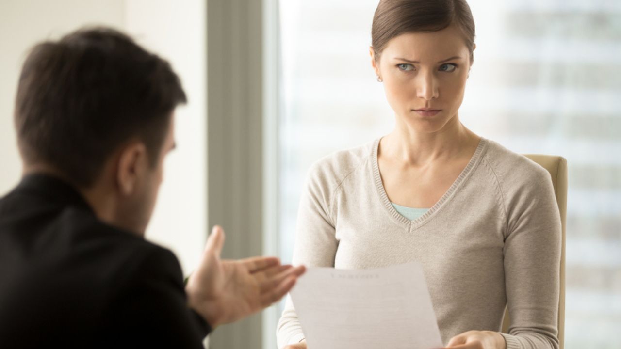 Millennial businesswoman with skeptical facial expression holding contract document and listening unconvincing offer of business partner. Suspicious terms of agreement, doubtful investor, fraud, scam