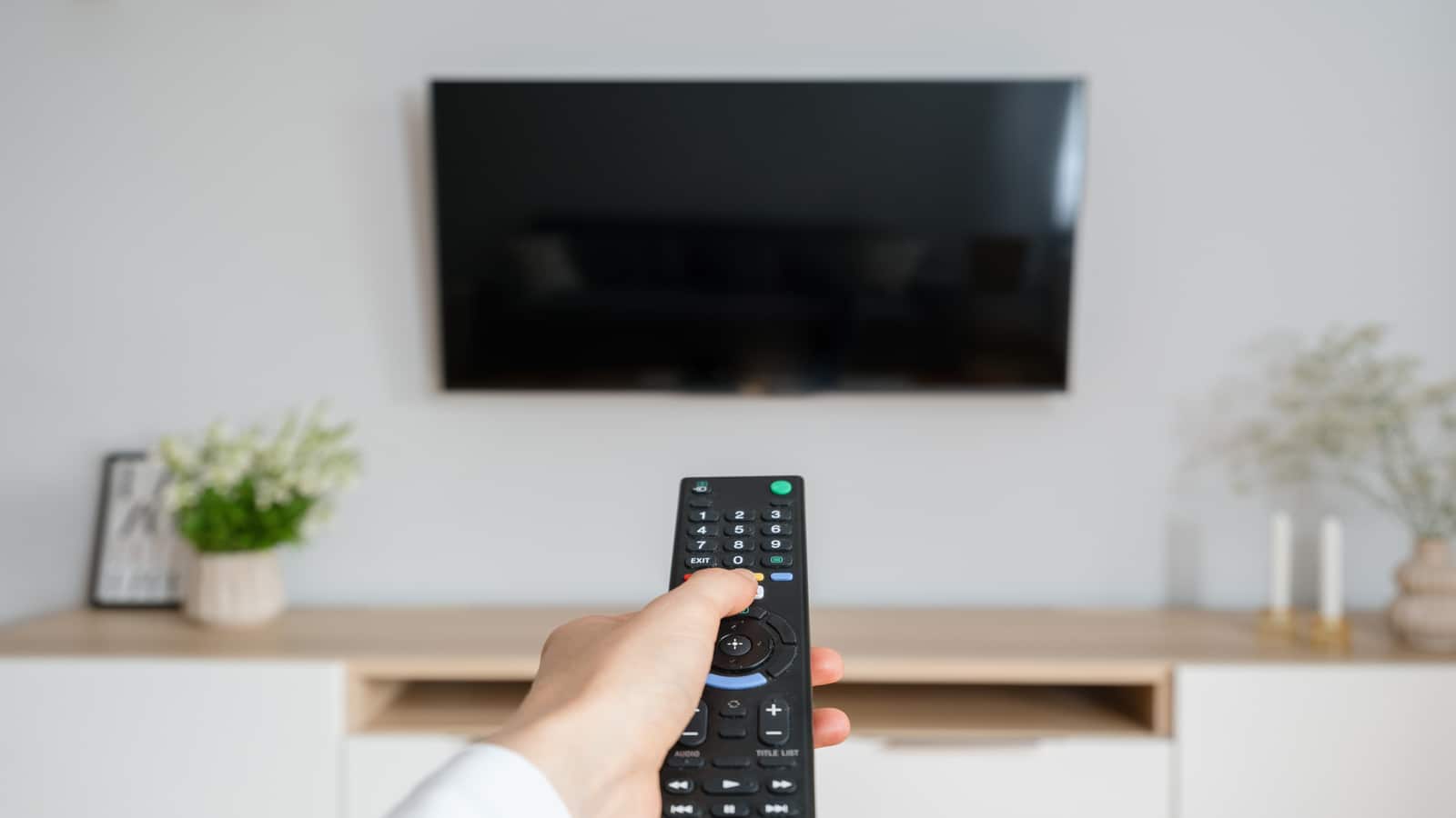 female hand hold tv remote control and press button to turn on television.