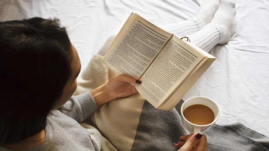 woman reading book and drinking coffee in bed in the morning.