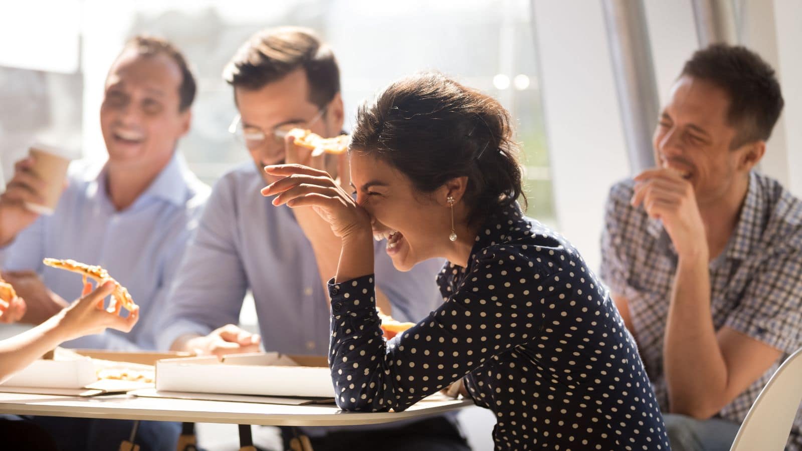 Colleagues laughing over a pizza lunch.