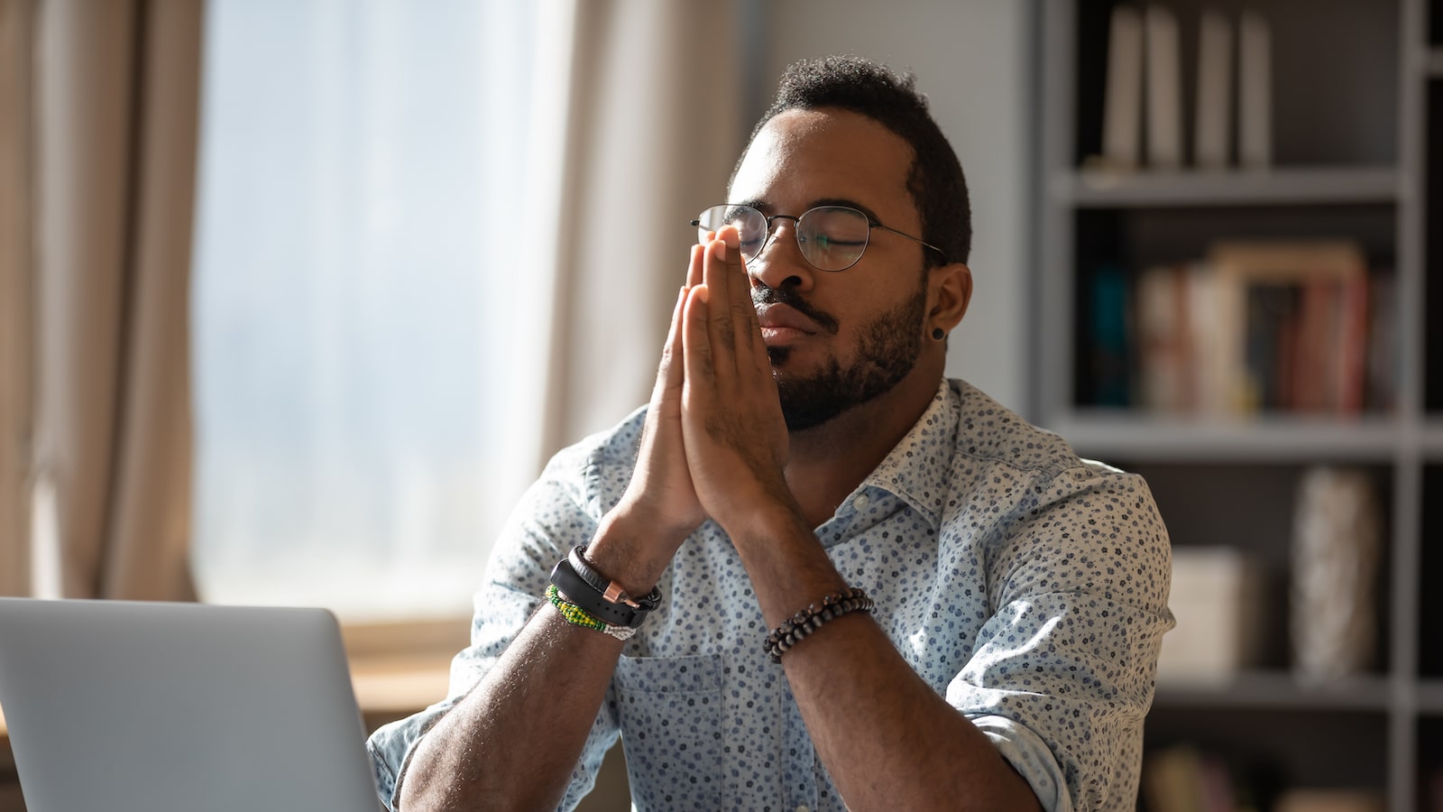 Man at his desk with clasped palms closed eyes thinking or reflecting.