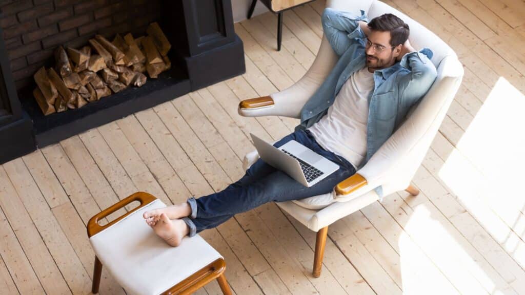 Peaceful young man resting with closed eyes in cozy armchair with laptop.