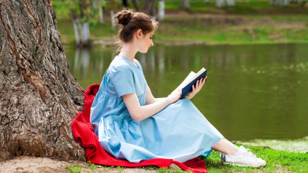 Young beautiful brunette girl reading a book in a summer park.