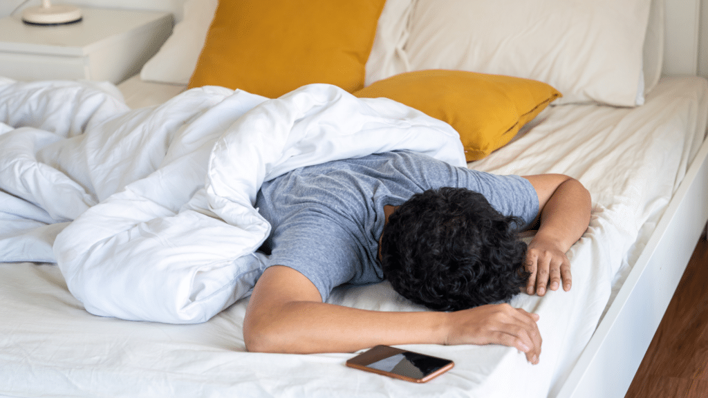 Young man sleeping on the bed and turning off smartphone alarm clock in the morning.