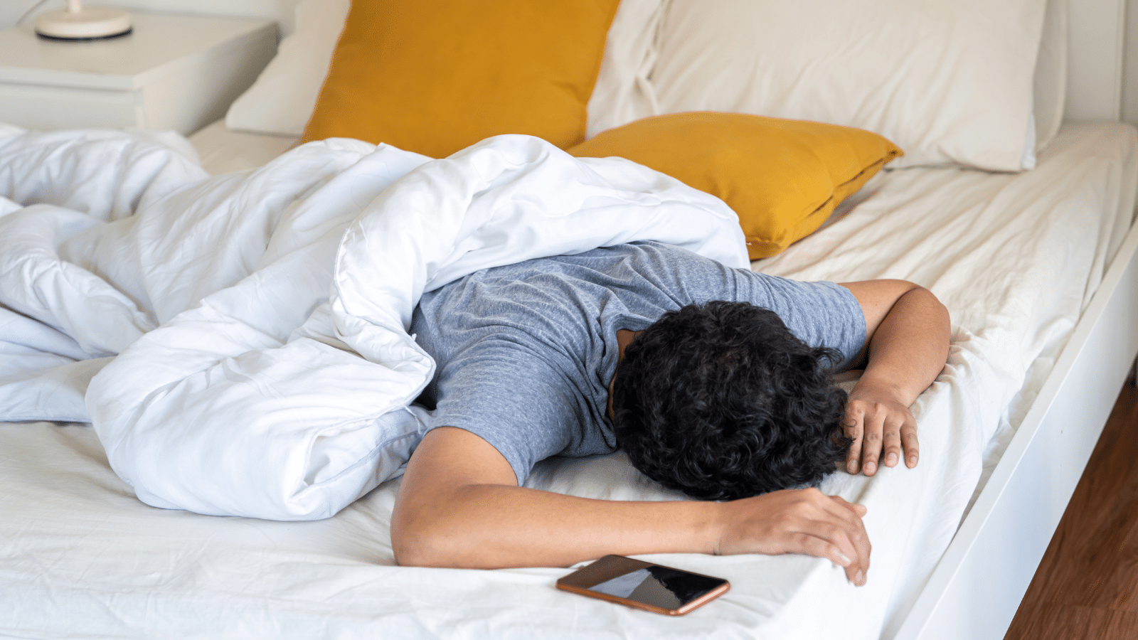 Young man sleeping on the bed and turning off smartphone alarm clock in the morning.