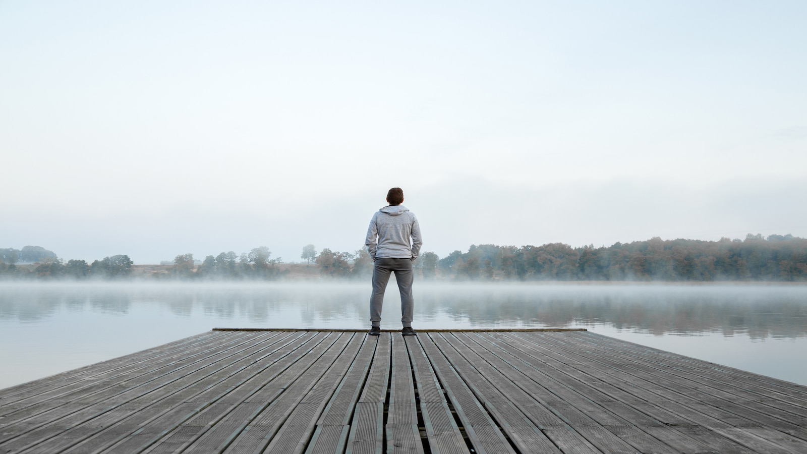 Man standing alone on wooden footbridge and staring at lake thinking about life.