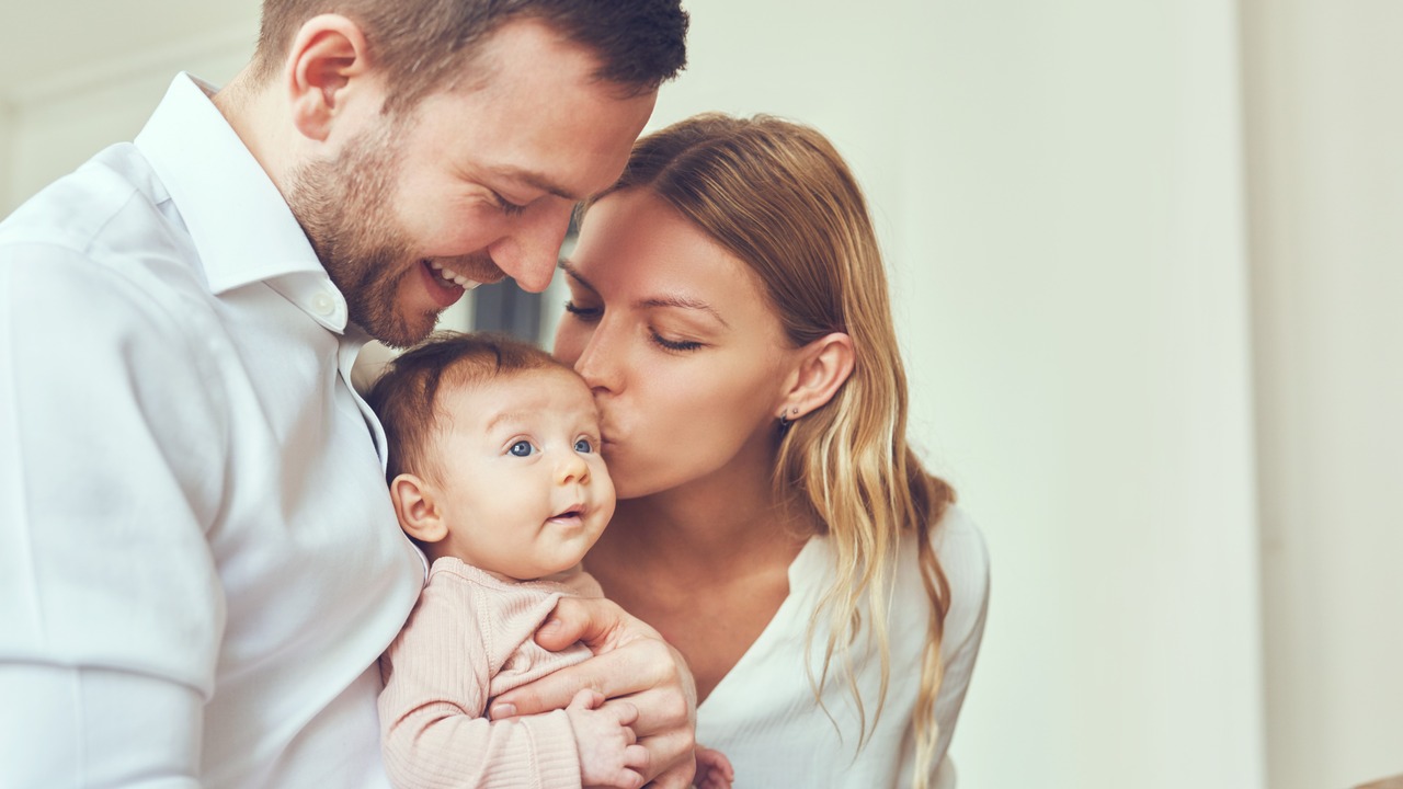 Smiling mother and father holding their newborn baby daughter at home.