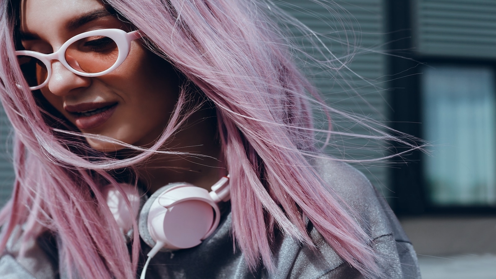 Beautiful young girl with purple pink hair listening to music on headphones, street style.