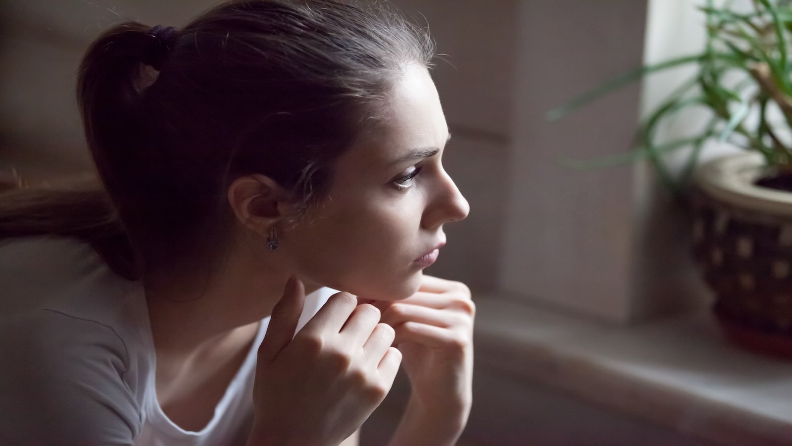 Upset young woman looking out window thinking.