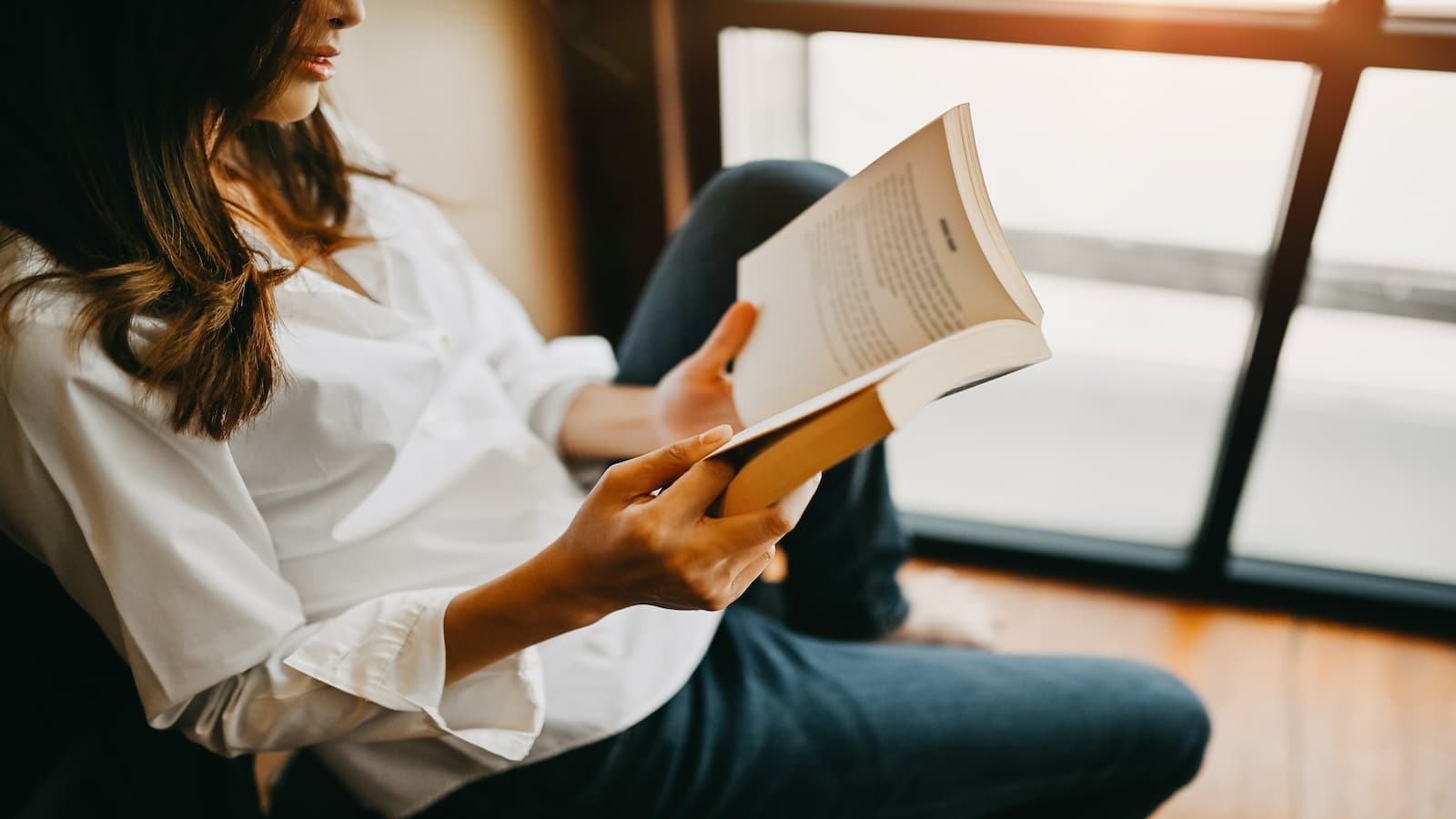 Woman reading book sitting on floor.