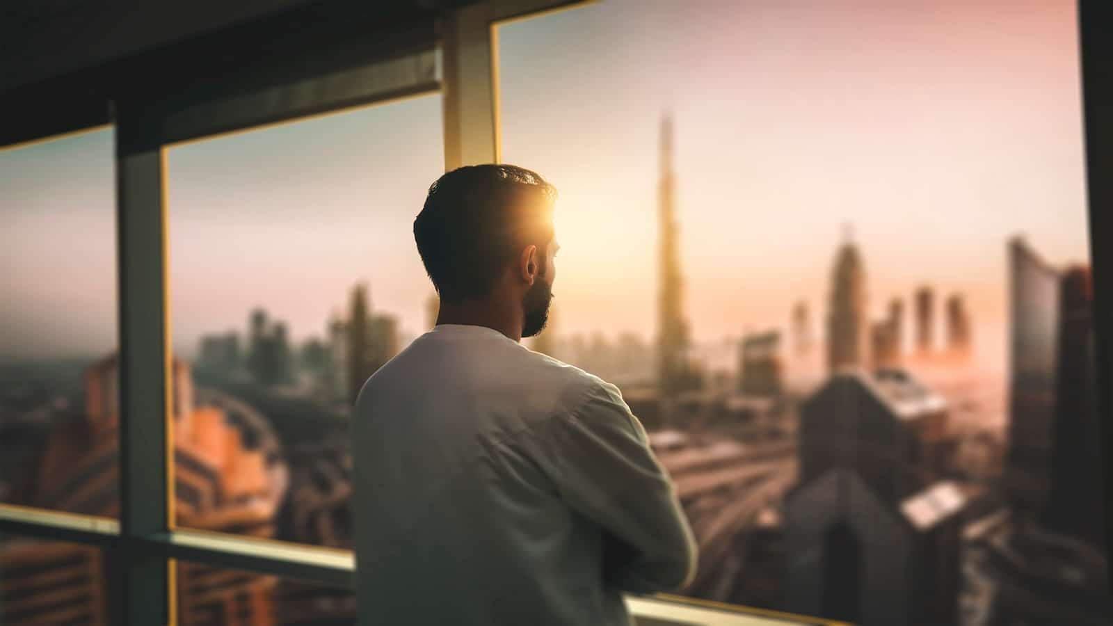 Young man looking at Dubai city through hotel window thinking.