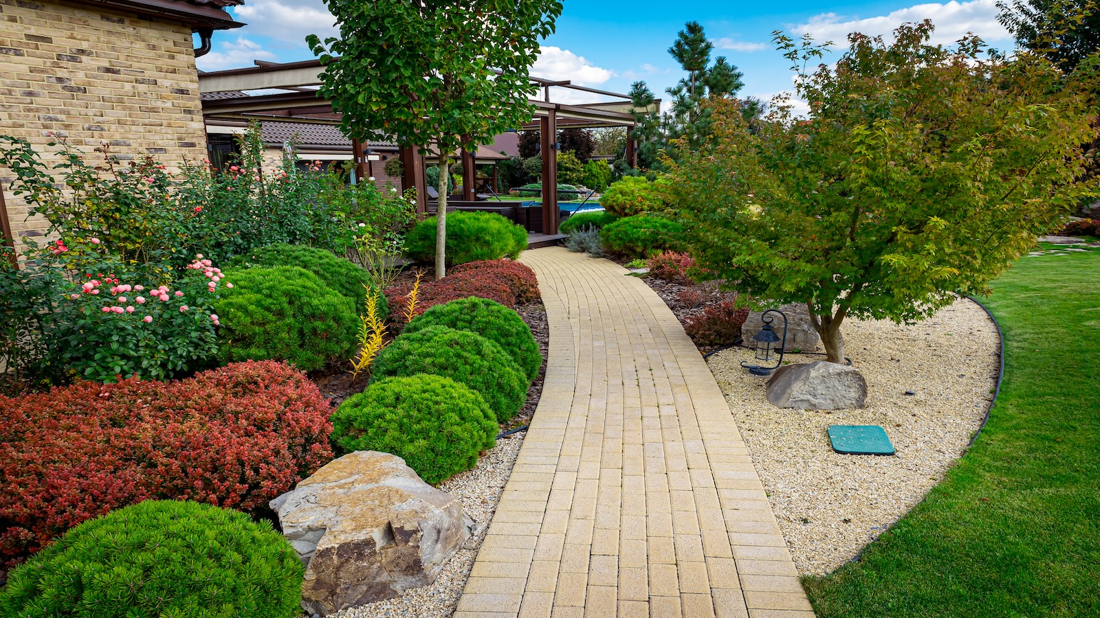 Front yard multicolored shrubs intersecting with bright green lawns behind the house is a modern, green grass