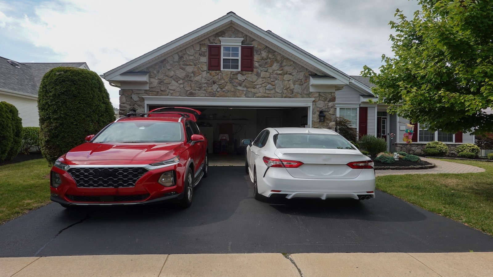 Driveway view of the stone facade of a house with two cars facing in different directions.