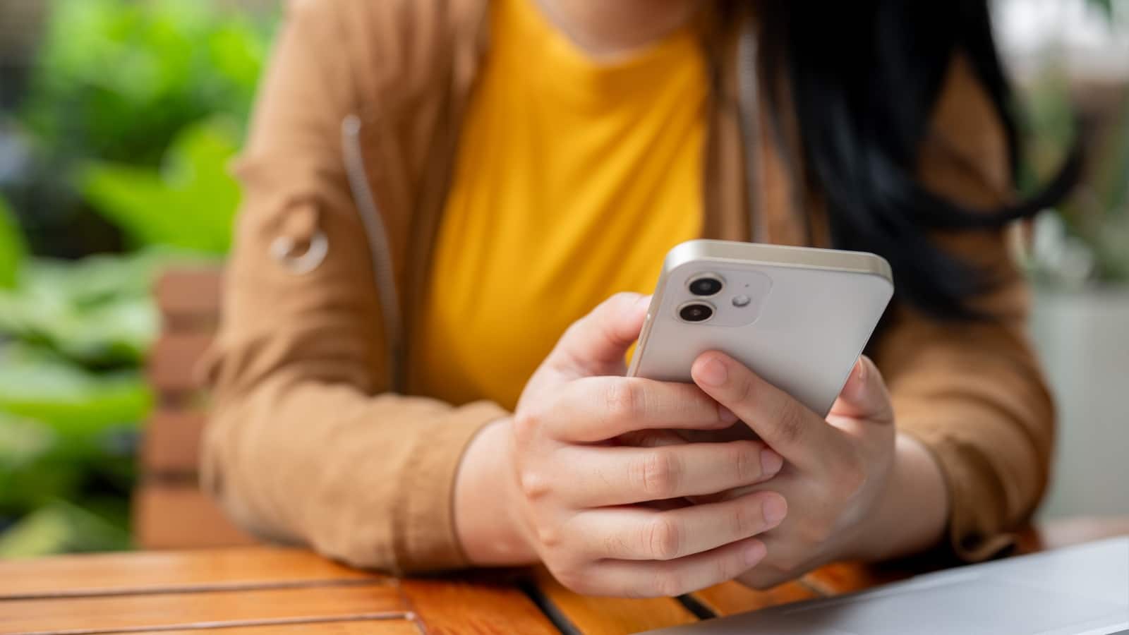 A cropped image of an Asian woman using her smartphone at a table while working remotely from a cafe. chatting, replying messages, scrolling on app, people and wireless technology concepts.