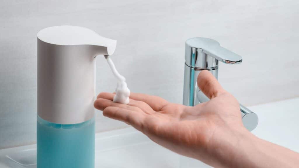Automatic soap dispenser in the bathroom. Hand with soapy solution closeup.