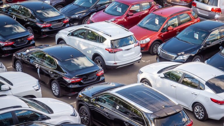 Sale of new and used cars in a dealership. Lots of cars in the car park. Black, white, silver and red cars of unknown brands. Cars in a lot, car dealership inventory.