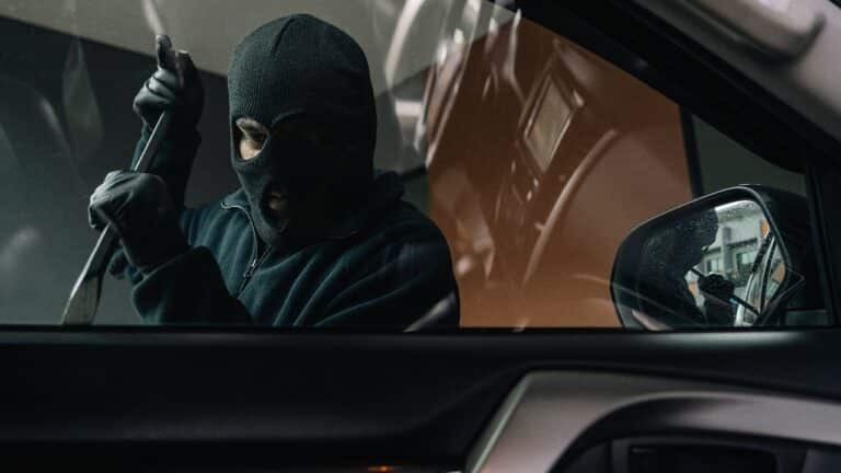 criminal with balaclava and crowbar breaking into a car window