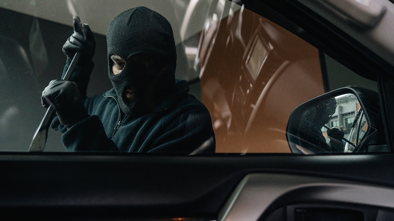 criminal with balaclava and crowbar breaking into a car window