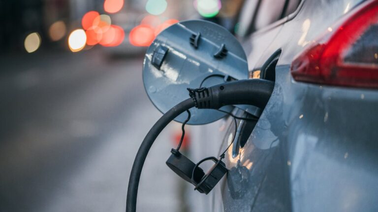 Close-up of an electric car charging. Traffic lights in a blurry background.