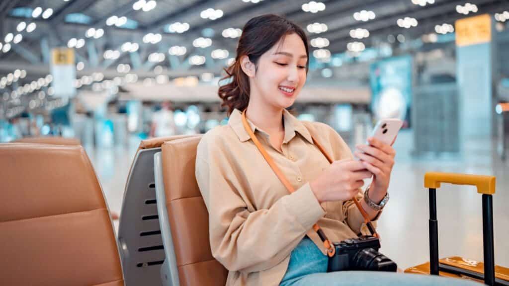 Happy asian tourist woman using mobile smartphone with suitcase traveling between waits for flight in Airport Terminal, Browse Internet, flight check in, Tourist journey trip concept.