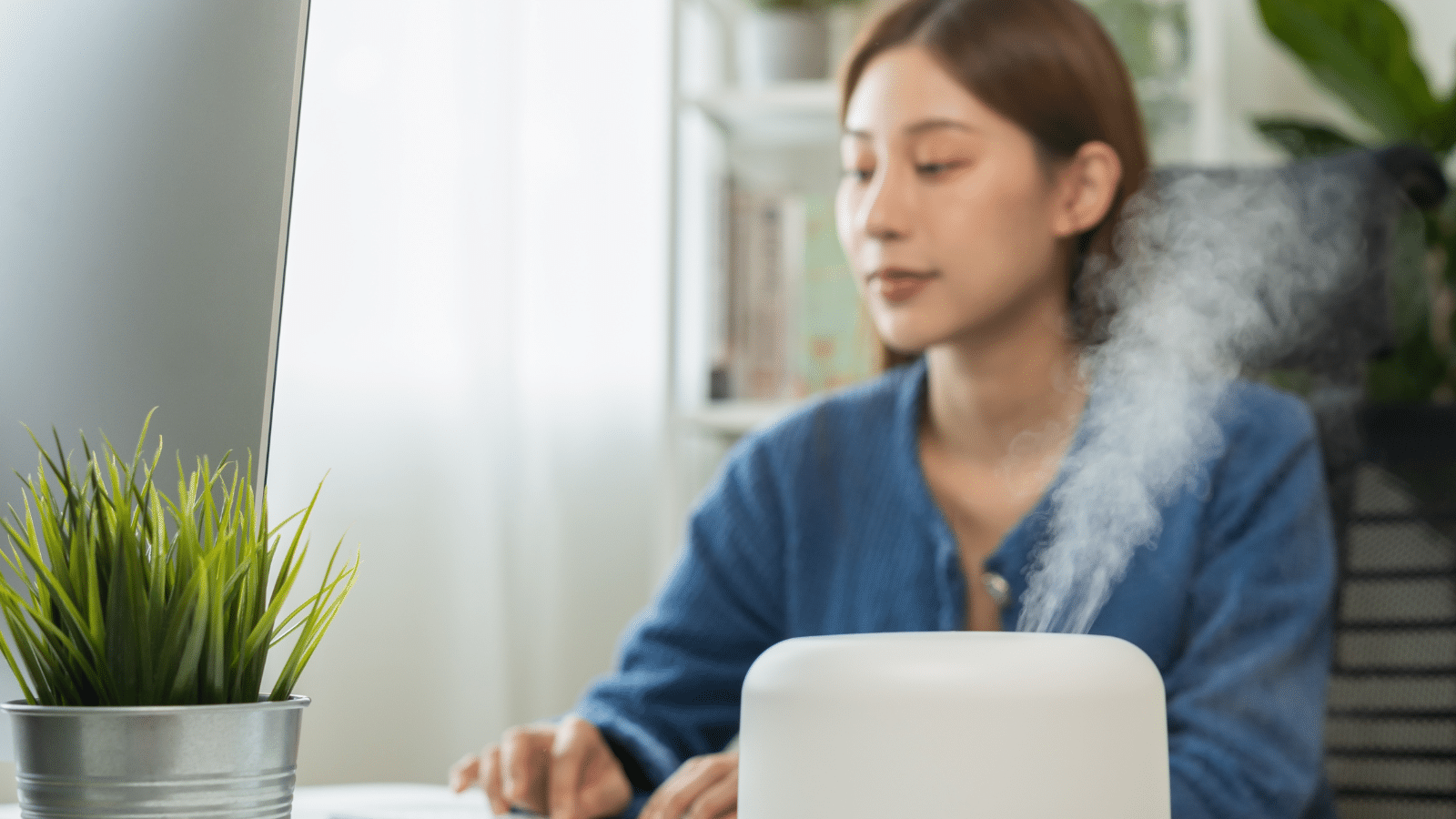 Woman enjoying enjoying aromatherapy steam scent from essential oil diffuser in room at home office.