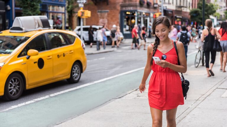 Woman walking in new york city using phone app for taxi ride hailing service or playing online game while commuting from work. Asian girl tourist searching for map directions on smartphone.